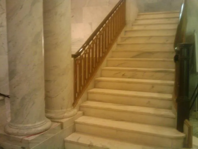 Broad indoor staircase with pale stone treads and a timber handrail