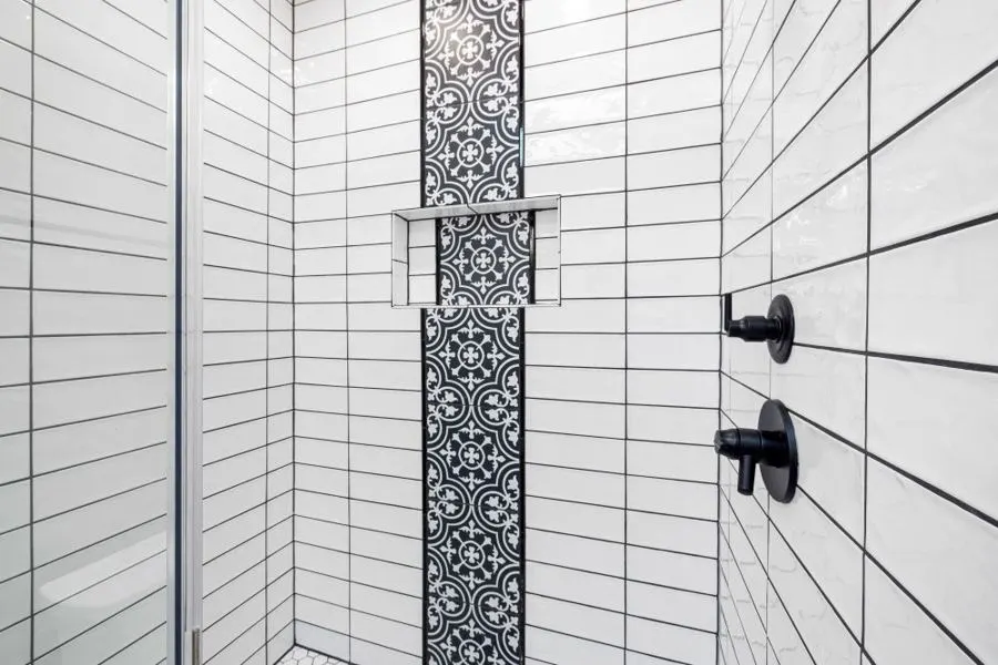 White shower tiles with a patterned vertical border and black fittings