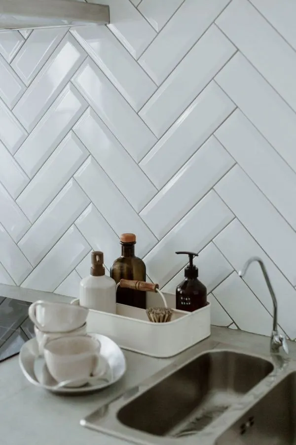 White herringbone kitchen backsplash beside a stainless steel sink
