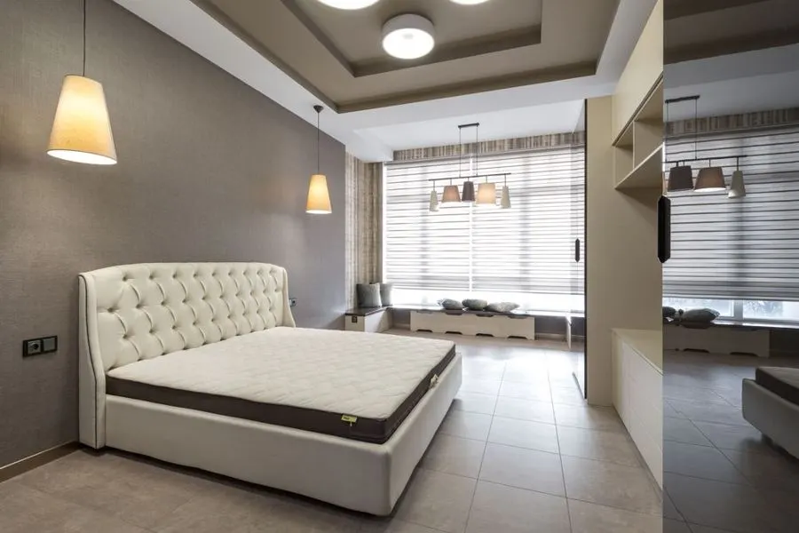 Bedroom with large grey floor tiles and a cream upholstered bed